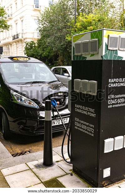 London, England - August 2021: London taxi fully\
powered by electric connected to an electric charing station on a\
city street.