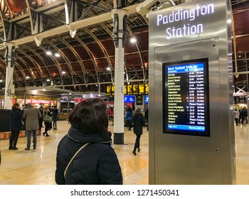 LONDON, ENGLAND - DECEMBER 2018: Persons checking a departures display screen at London Paddington Station.