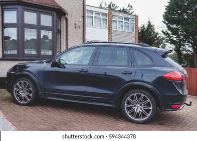 LONDON, ENGLAND - FEBRUARY 28, 2017: Black Porsche Cayenne S Parked On A Red Cobbled Driveway Next To A House In Suburban Area In London, Side View.