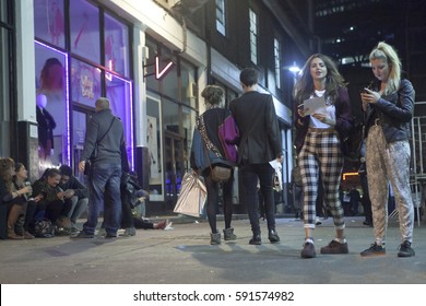 LONDON, ENGLAND - JULY 12, 2016 Girls Go On Brick Lane. Night. People Are Sitting On The Sidewalk, Drinking Alcoholic Beverages And Communicating