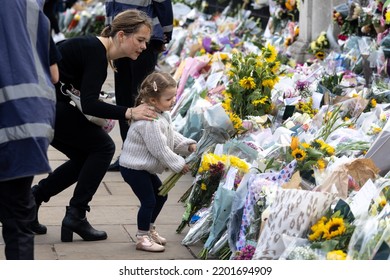 LONDON, ENGLAND - SEPTEMBER 9, 2022: A Child With Her Mother Lays A Bunch Of Flowers At The Gates Of Buckingham Palace In London On September 9, 2022, In Tribute To Queen Elizabeth II Who Died The Day