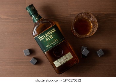 London, England, UK - 21 March 2021. Tullamore Dew is a branded Irish Whiskey. Whiskey bottle, glass and stones under a wooden backdrop.