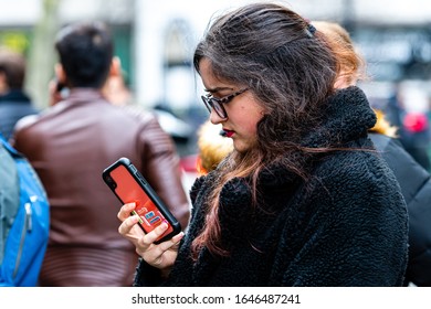 London, England, UK - January 2, 2020: Young Woman With Glasses Standing In Crowd Of People Staring At Smartphone