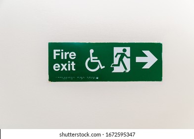 London, England, UK - March 11, 2020: A Neon Green Exit Sign Plate With A Disabled, Man Figure And Arrow To The Door As An Instruction For Directions In Case Of An Emergency
