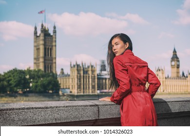 London fashion week Asian model woman at Westminster parliament, iconic british landmark Big Ben city background. Autumn trend lady wearing red trench coat rain outerwear. Europe travel lifestyle.