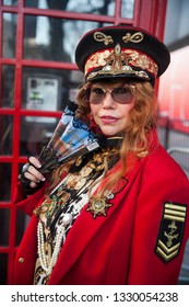 LONDON - FEBRUARY 15, 2019: Stylish Attendees Gathering Outside 180 Strand For London Fashion Week. Woman In Military Cap, Red Jacket With American Flag, Skirt , High Boots, Posing At Telephone Booth