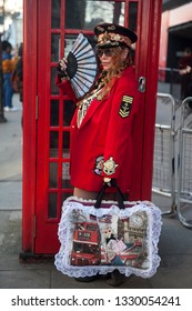 LONDON - FEBRUARY 15, 2019: Stylish Attendees Gathering Outside 180 Strand For London Fashion Week. Woman In Military Cap, Red Jacket With American Flag, Skirt , High Boots, Posing At Telephone Booth