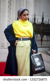 LONDON - FEBRUARY 15, 2019: Stylish attendees gathering outside 180 The Strand for London Fashion Week. A girl in a yellow sweater and a narrow pencil skirt, black coat - Shutterstock ID 1332726875
