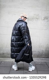 LONDON - FEBRUARY 17, 2019: London Fashion Week. Blonde Man Wears Clear Pvc Belt Bag, Black Down Jacket And Grey Trousers, White Sneakers With Saunt Lauren Bag