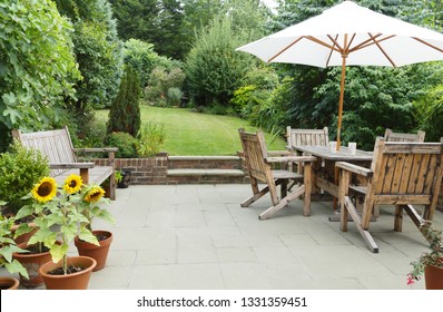 London garden in summer with patio, wooden garden furniture and a parasol or sun umbrella - Shutterstock ID 1331359451
