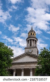 London, Great Britain - July 3, 2022: Closeup Of Clock Tower With Golden Caryatid Statues And Pediment On Columns Of St. Marylebone Parish Church Under Blue Cloudscape. Green Foliage 