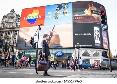 LONDON- JULY, 2019: London street scene with people walking in front of the Piccadilly Lights, a famous landmark / giant advertising screen on Piccadilly Circus