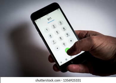 London, London/UK - April 02 2019: IPhone Being Used To Dial Emergency Phone Numbers, 999, 911, 112 White Background With Mans Hand Holding Mobile Or Cell Phone