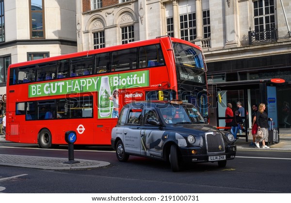 LONDON - May 18, 2022:\
Black cab turning in front of red Double Decker Bus at bus stop on\
The Strand, London