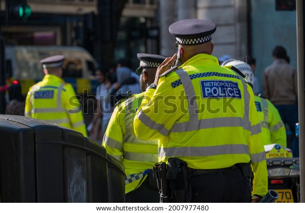 LONDON - MAY 29, 2021: British\
police officer in a high visibility jacket uses a mobile cell\
phone