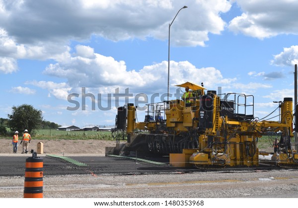 London, ON - August 2019: Construction site\
on a highway during summer time. Asphalt paver machine building a\
new road. Operators on site. Lane\
closure.