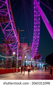 LONDON - SEPTEMBER 14, 2021: The Lower Half Of The London Eye With People Passing By At Night. Colourfully Illuminated.