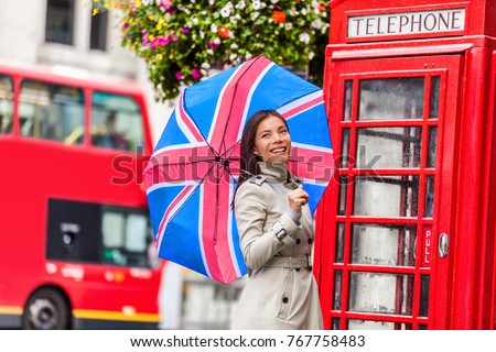 London tourist travel woman with UK flag umbrella, telephone box, red big bus. Europe travel destination Asian girl with british icons, red phonebox, double decker hop on hop off bus in famous city.
