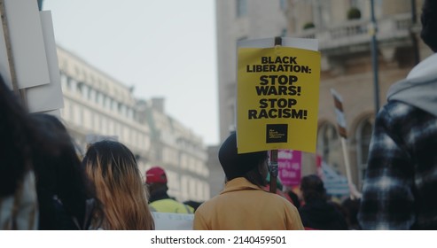 London, UK -03 19 2022: Woman protester in crowd holding a sign at Portland Place, ‘Black Liberation: Stop Wars! Stop Racism!’, for the yearly ‘March Against Racism’, held around ‘UN Anti Racism Day’.