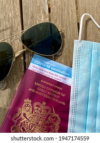 London, UK - 03.31.2021: Covid 19 Vaccine Passport Concept  For Restrictions On Travel With Sunglasses, UK Passport And Covid Mask And Vaccine ID Card 