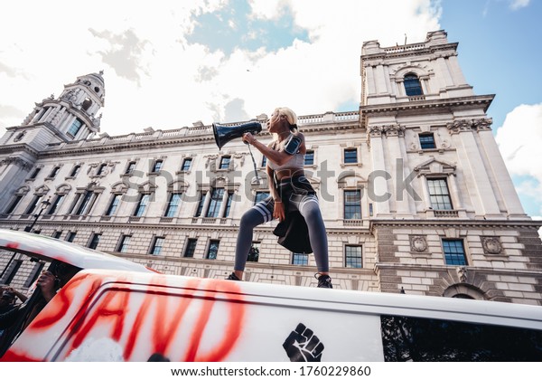 London / UK - 06/20/2020: Beautiful girl with\
megaphone standing on the top of the van in front of the Huge crowd\
of Black Lives Matters protesters heading to Parliament Square,\
Westminster
