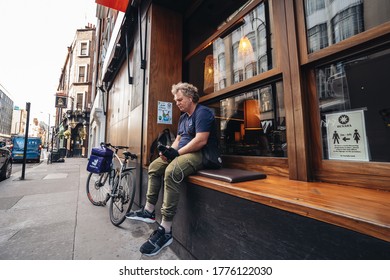 London / UK - 07/11/2020: Food Delivery Driver Sitting On The Busy Restaurant Terrace In Soho Area During Coronavirus Lockdown Ease