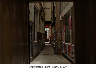 London, UK - 09/02/2020: Two Blurred People Walking Past An Alleyway In Soho With Posters On The Walls And A Neon Sign At The End.