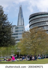 London, UK - 1 May 2021: Londoners Enjoy Socially Distanced Outdoor Yoga Class In A Grass Park Close To Iconic City Buildings. They Sit Below The Unique Architecture Rising High Above The Trees. 