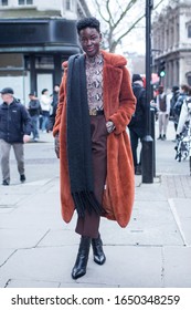 London, UK - 13 February, 2020, Street style. A girl in a faux fur red fur coat, a turtleneck with a snake pattern, a black scarf, brown short culottes and a Moschino belt poses outdoors.