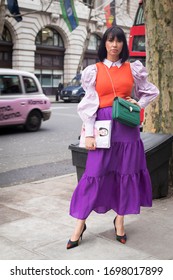 London, UK - 15 January 2020 Fashionable people on the street . Street style. Brunette girl with long hair in a long lilac skirt, orange vest and white clutch blouse