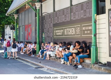 London, UK - 16 July, 2022 - Row Of Tourists Sit On Kerbside As They Have Takeaway Street Food At Borough Market