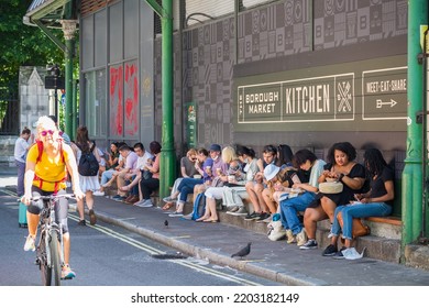 London, UK - 16 July, 2022 - Row Of Tourists Sit On Kerbside As They Have Takeaway Street Food At Borough Market