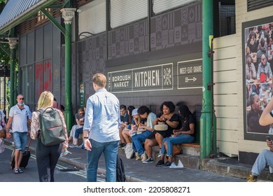 London, UK - 16 July, 2022 - Row Of Tourists Sit On Kerbside As They Have Takeaway Street Food At Borough Market