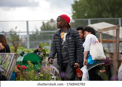 London, UK - 17 July 2019, Nomadic Community Garden. Communal Garden Party. A Young Man In A Black Denim Suit With Dreadlocks Is Walking Around The Garden