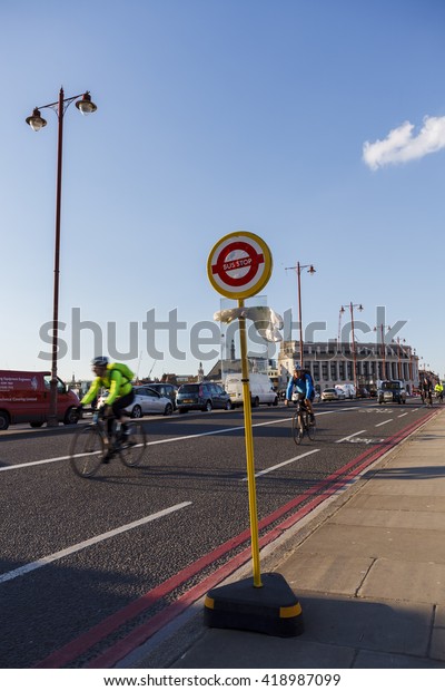 LONDON, UK -\
2016.03.31: Bus Stop sign on the Blackfriars Bridge, cyclists in\
the background.\
Bright sunny\
day.