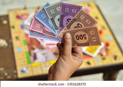 London, UK, 2020. Player Holding And Neatly Arranging Fake Money / Currency Notes In His Hand With The Monopoly Board Game In The Background. Playing At Home In Quarantine During Lockdown 