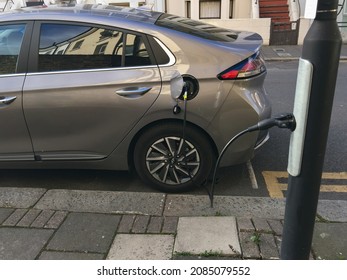 London, UK - 2021 Dec. 1: An Electric Car Parked In A Street In A Residential Area Of South London Is Hanging By Being Plugged Into A Socket On A Lamp Post With A Black Charging Cable.