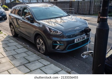 London, UK - 2022 March 7: A Black Electric Car Parked In A Street In A Residential Area Of South London Is Plugged Into A Public Charging Point On A Lamp Post With A Charging Cable.