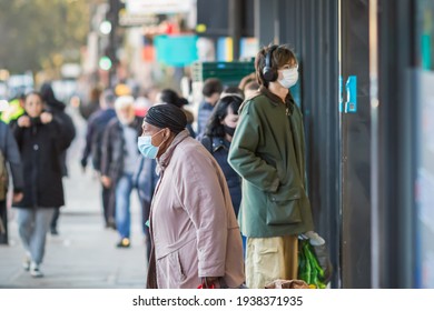 London, UK - 26 February, 2021 - A black woman with a face mask leaving the shop and a queue in the background during the COVID-19 pandemic
