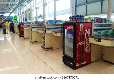 London, UK - 28 August 2018: Coke Cooler Fridge At The End Of A Long Aisle Of Checkout Till Register Counters In A Supermarket.