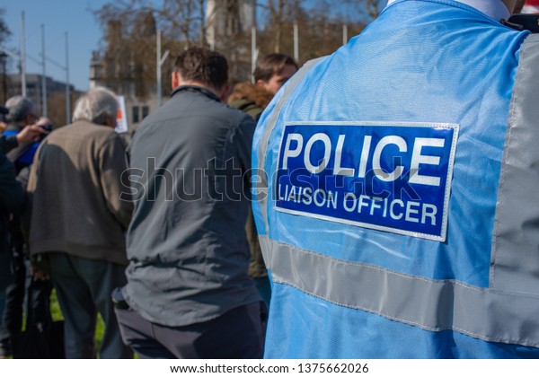 London,\
UK. 29th March 2019. Metropolitan Police Liaison Officer wearing\
blue reflective vest, watches protesters at a Brexit day rally\
being held in Parliament Square, central\
London.