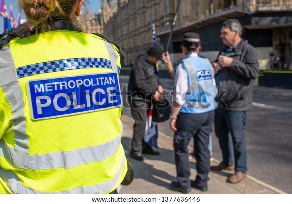 London, UK. 29th March 2019. Metropolitan Police\
Officer in the foreground, watches on as a Police Liaison Officer\
deals with two protesters at the March For Leave rally in\
Parliament Square,\
London.