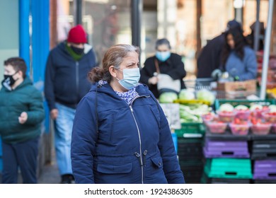 London, UK - 5 February, 2021 - A Senior Woman Wearing A Protective Face Mask Passing By An Outdoor Produce Market On Wood Green High Street