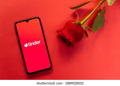 London, UK - 6 january 2021: tinder dating app logo on mobile phone with face mask and red rose. Concept of dating during covid19 pandemic. Romantic flat lay on red background