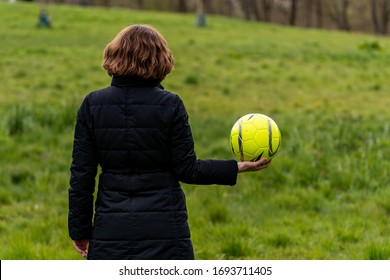 London, UK - April 04 2020: A Woman In Black Uniform Holds A Yellow Football / Soccer Ball. A Green Field As A Background. 