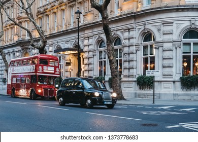 London, UK - April 13, 2019: Black Cab And An Afternoon Tea Bus Tour Inside Retro Red Double Decker Bus On A Street In London, UK, At Dusk. Double Decker Bus Is An Iconic Symbol Of The City.