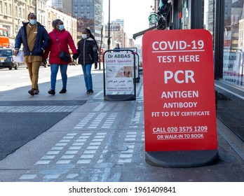London, UK - April 24, 2021: PCR and antigen covid-19 test sign in a London street. Pharmacy offering fit to fly certificates. Family with face masks passing by.