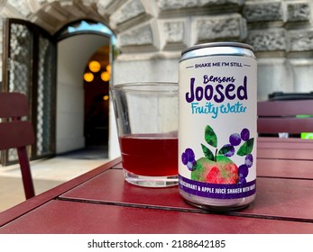 London, UK - August 1, 2022: A Selective Focus Shot Of A Can Of Bensons Joosed Fruity Water Drink Placed On An Outdoor Wooden Table Next To A Partially Filled Glass.