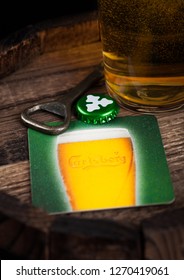 LONDON, UK - AUGUST 10, 2018: Carlsberg beer coaster with bottle top and opener and glass of beer on top of wood barrel.