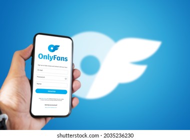 London, UK, August 2021; a hand holds a mobile phone with the OnlyFans registration form on the screen and the logo blurred in the background.